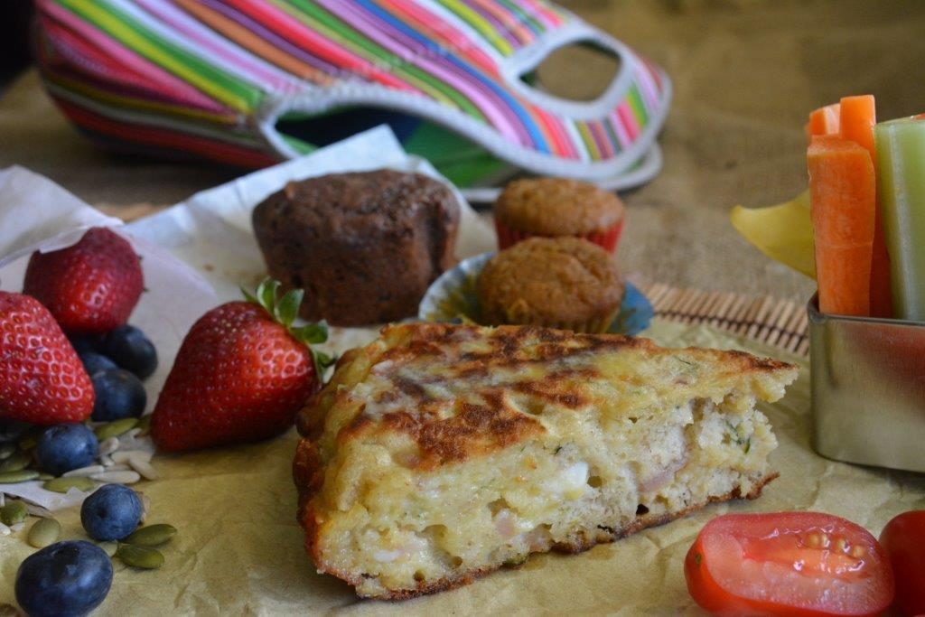 Zucchini, bacon and feta quickbread from with fruit, vegetables and a lunchbox in the background