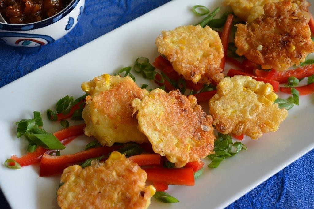Gluten-free corn fritters on a white platter with red capsicum and green spring onions. Top 10 gluten-free lunch recipes