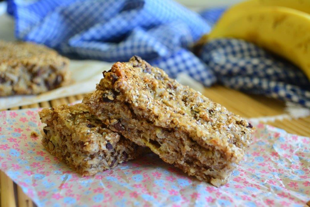 Gluten-free banana breakfast bars on multi-coloured wax paper, with blue checked cloth in background