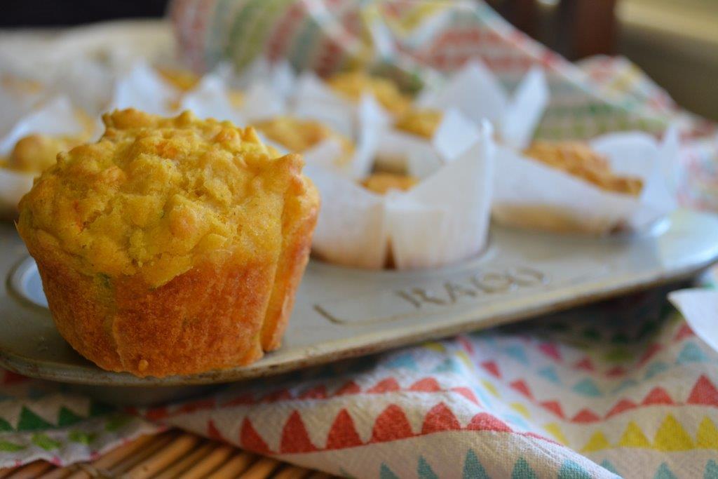 Gluten-free cheesy carrot and zucchini muffins with multicoloured tea towel in foreground