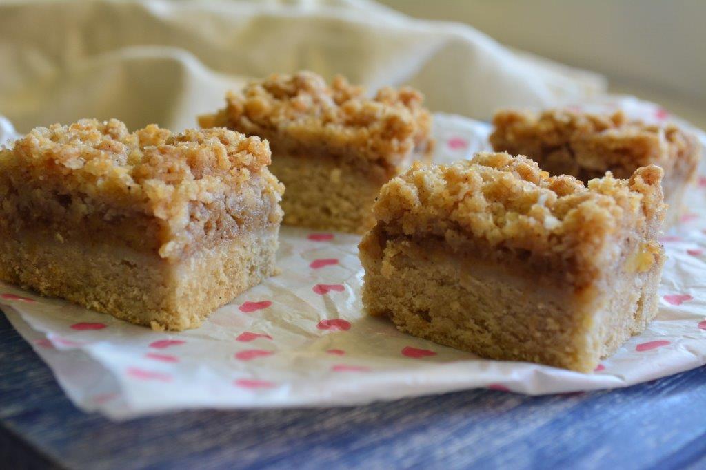 Gluten-free apple slice with crumble topping on pink spotted baking paper and blue wooden tray