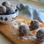 Gluten-free chocolate apricot balls in a bowl in background with balls scattered on a board in foreground.