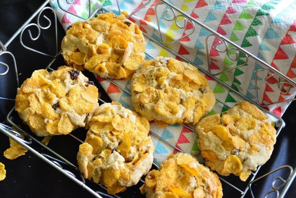 Six gluten-free cornflake cookies in wire basket with multicoloured tea towel, flat-lay view