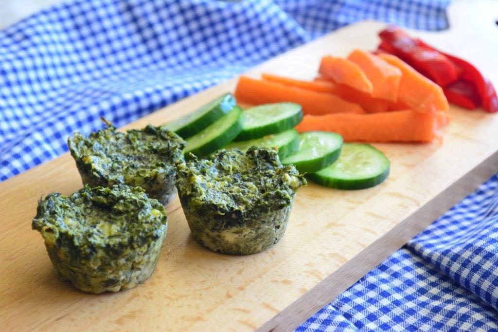 Gluten-free spinach and feta bites on a board with cucumber, carrot sticks and red capsicum