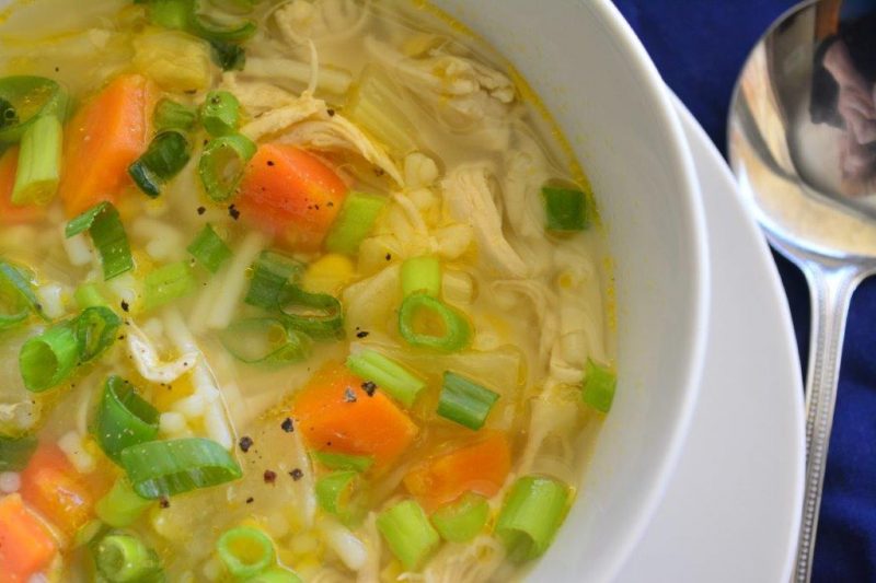 Bowl of gluten-free chicken vegetable soup with noodles, on a plate with a soup spoon
